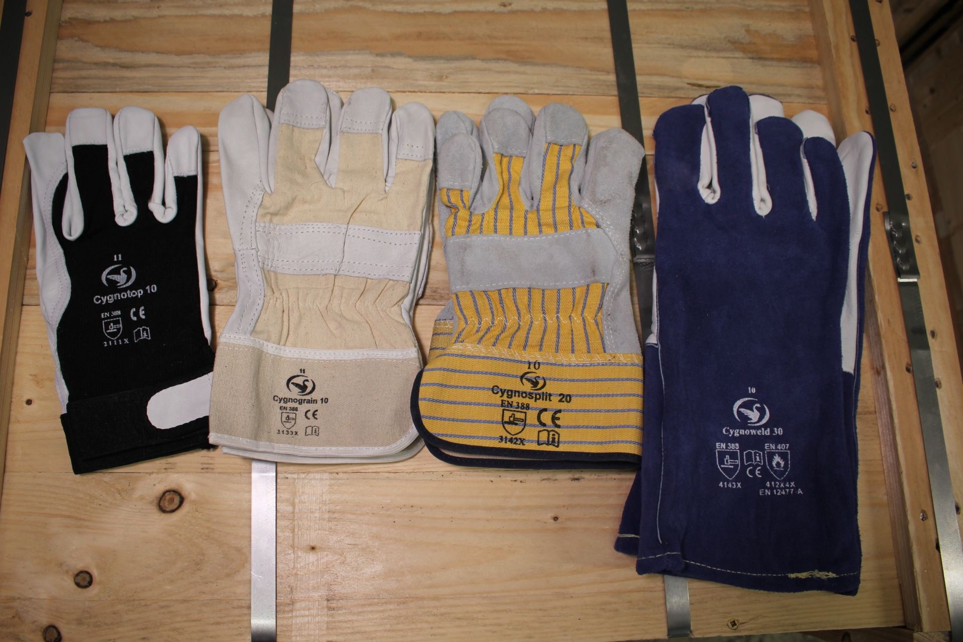 Auswahl an unterschiedlichen Leder-Arbeitshandschuhen, präsentiert auf einer Holzbox. Ziegenleder- und Rindnarben- und Spaltlederhandschuhe
